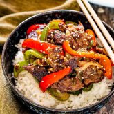 asian pepper steak over a bed of rice in a bowl.
