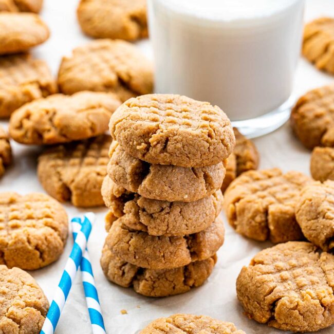 a stack of peanut butter cookies in front of a glass of cold milk.