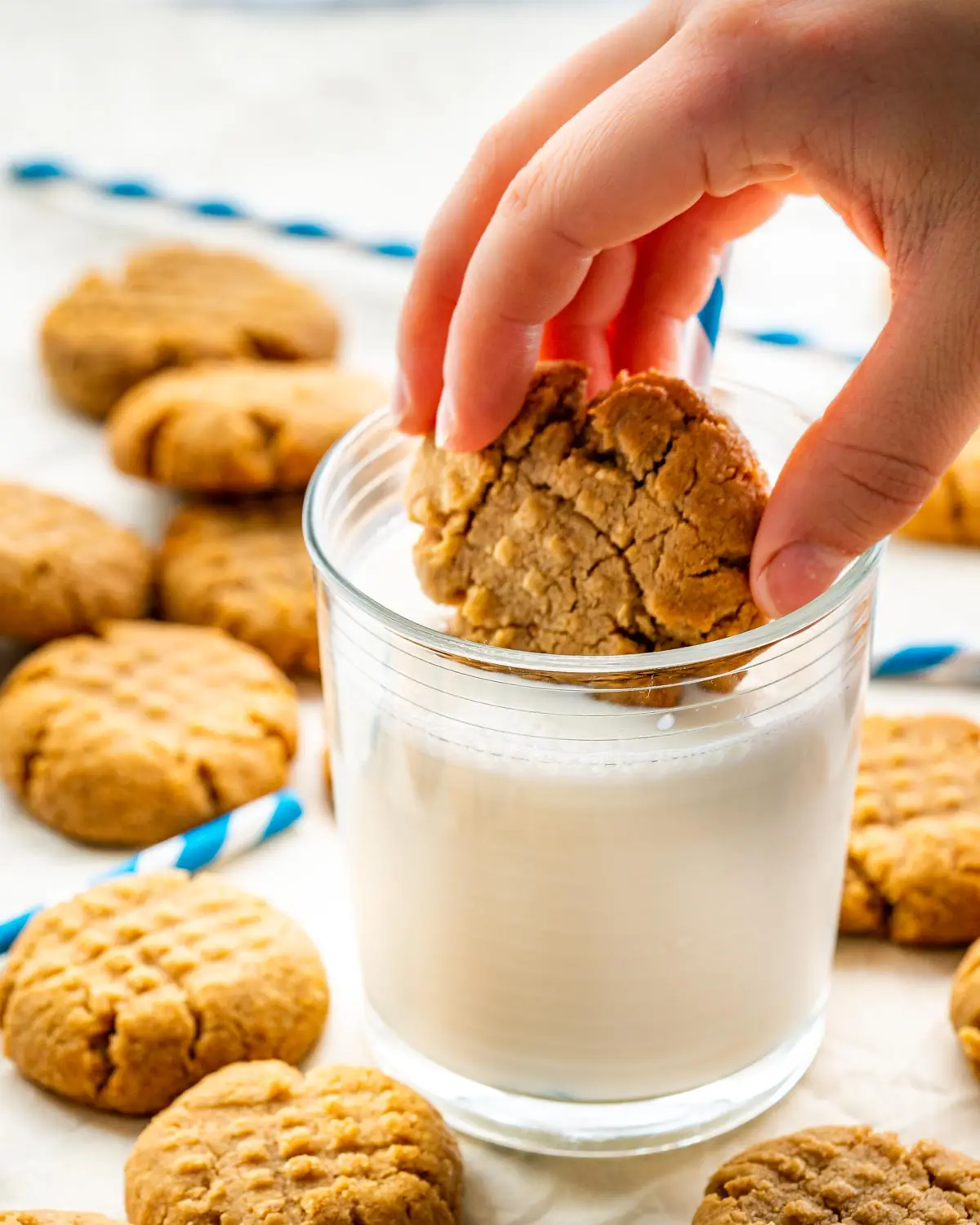 a hand dunking a peanut butter cookie in a glass of cold milk.