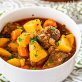 a white bowl filled with beef stew and garnished with parsley.