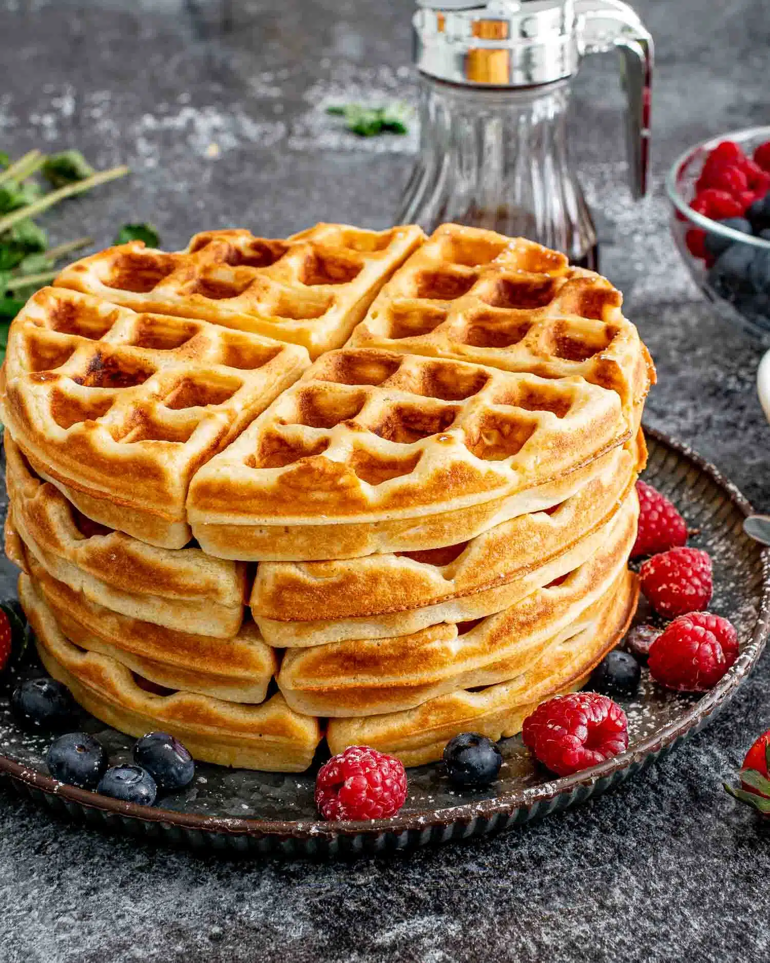 a stack of waffles on a metal plate surrounded by some berries.