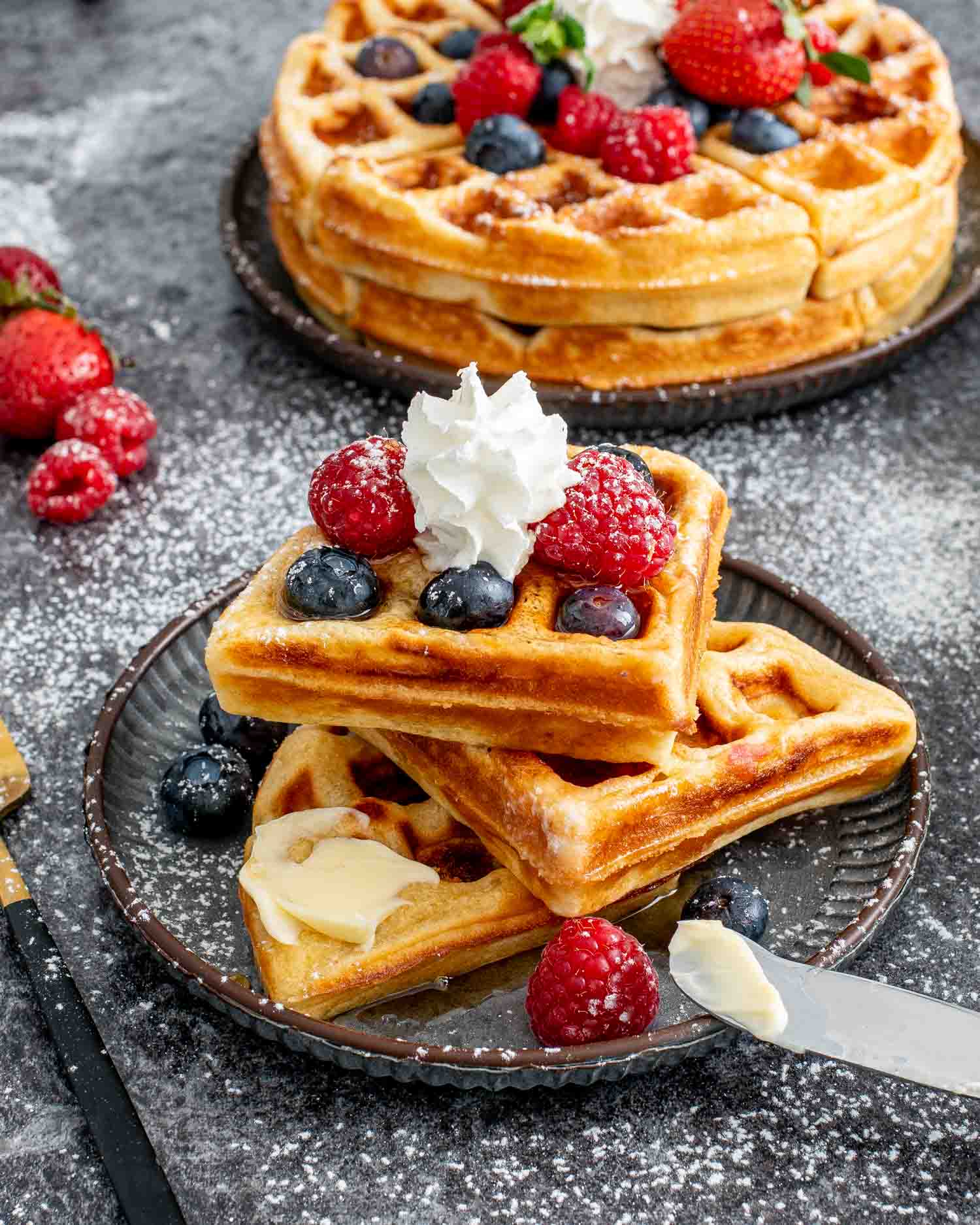 a few pieces of waffles on a plate topped with berries, whipped cream and butter.