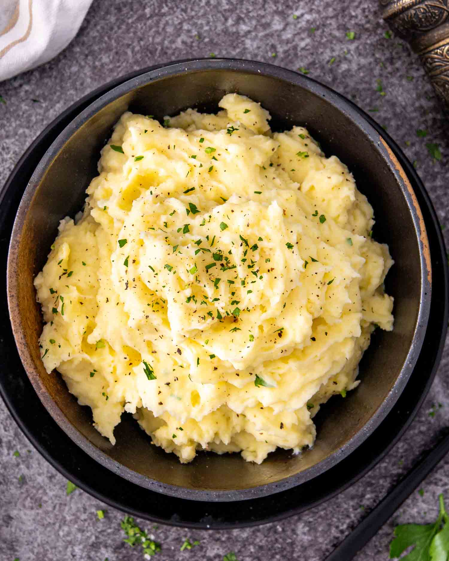 a black bowl loaded with freshly made mashed potatoes garnished with a bit of parsley.
