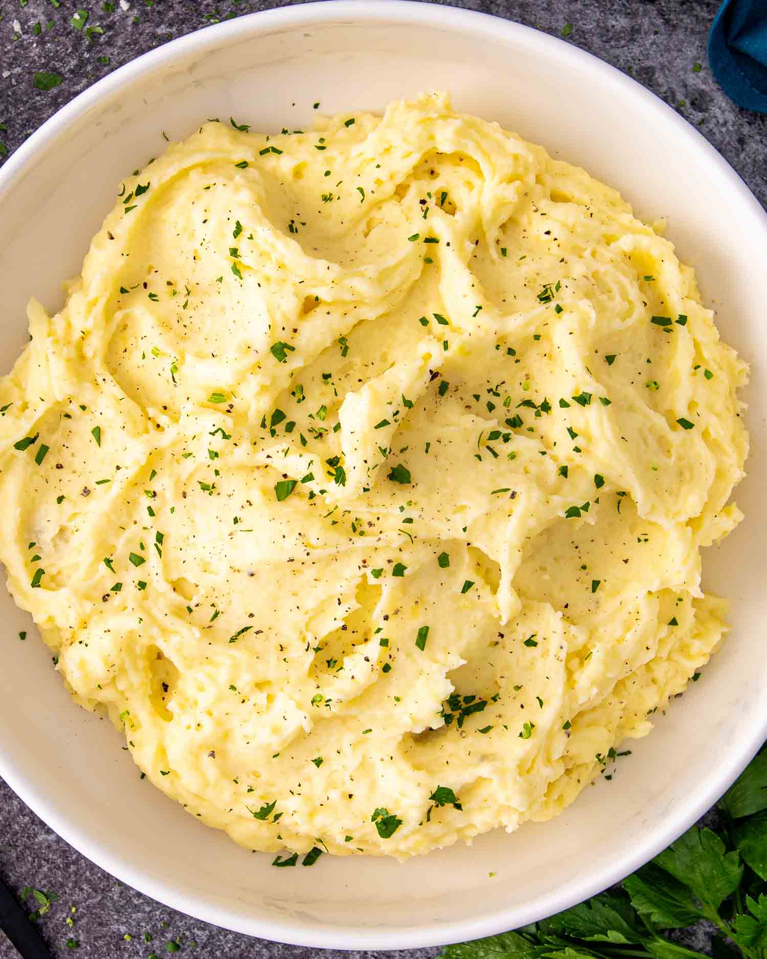 a big white bowl with freshly made mashed potatoes and garnished with a bit of parsley.