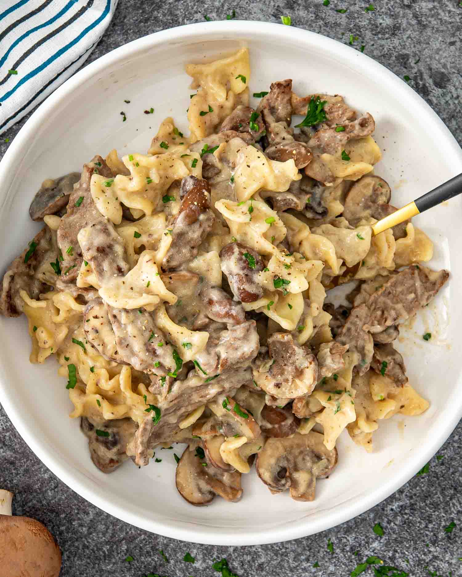 a white bowl with a serving of beef stroganoff garnished with a bit of parsley.