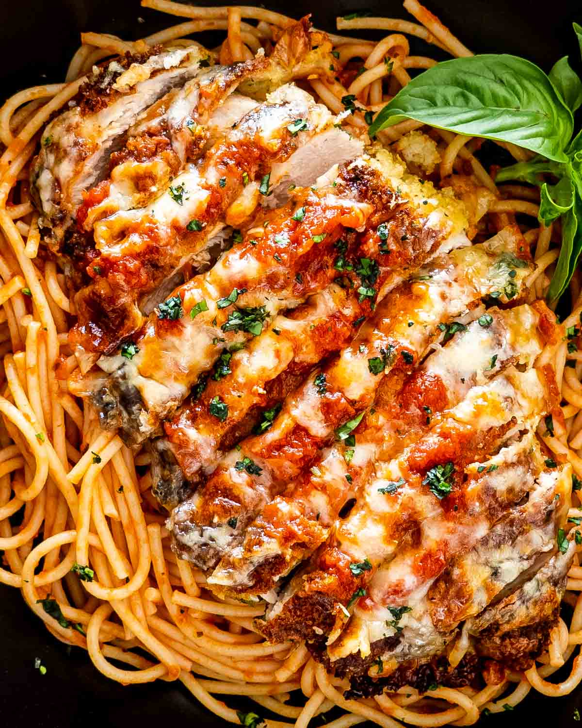 sliced up chicken parmesan on a bed of spaghetti in a black bowl.