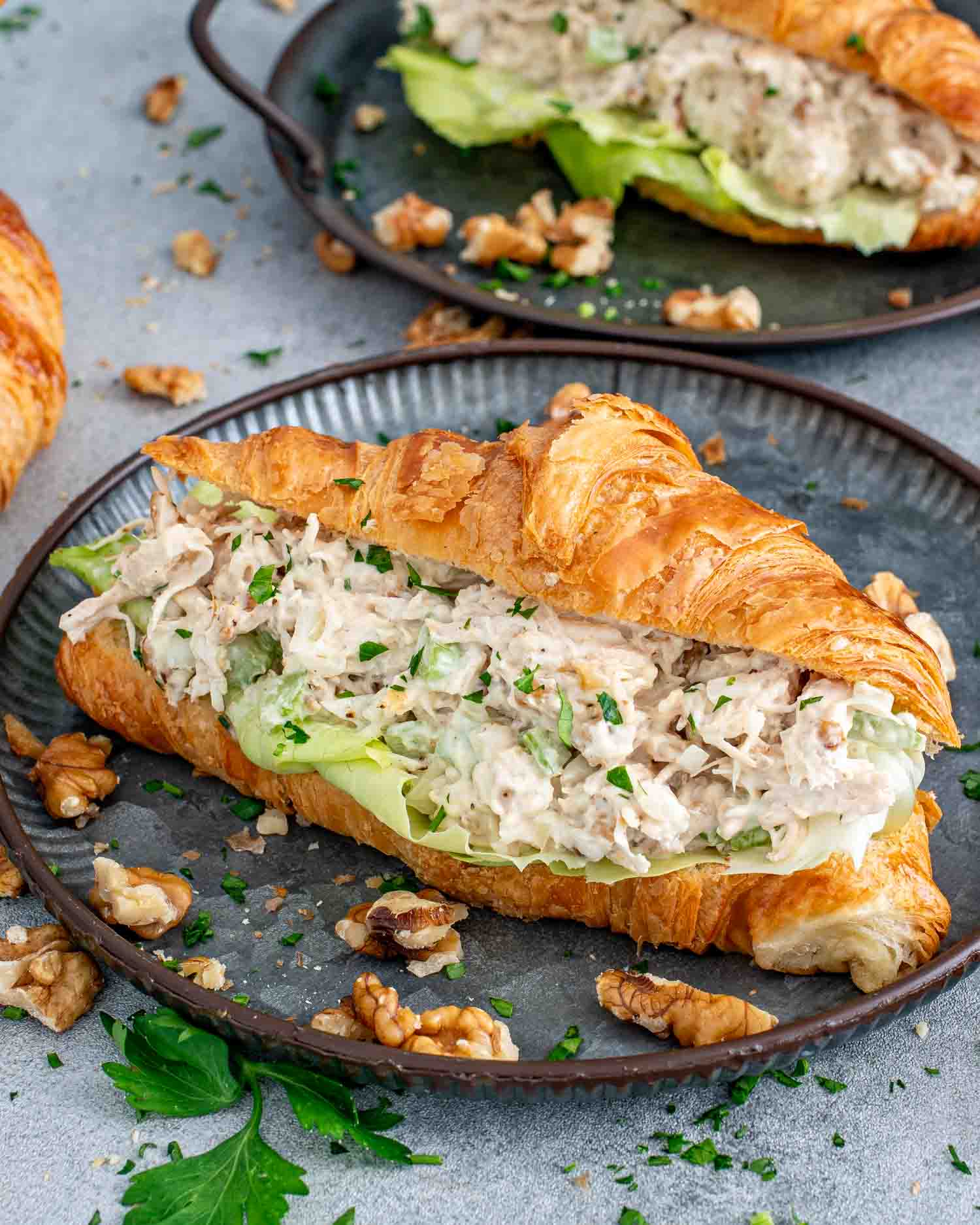 a chicken salad croissant sandwich on a plate garnished with a few walnuts.