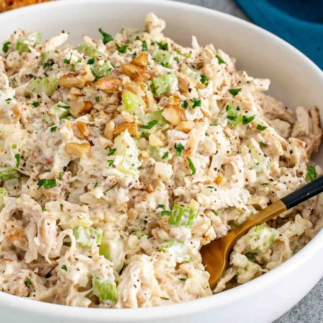 freshly made chicken salad in a white bowl garnished with a few extra crunchy walnuts.