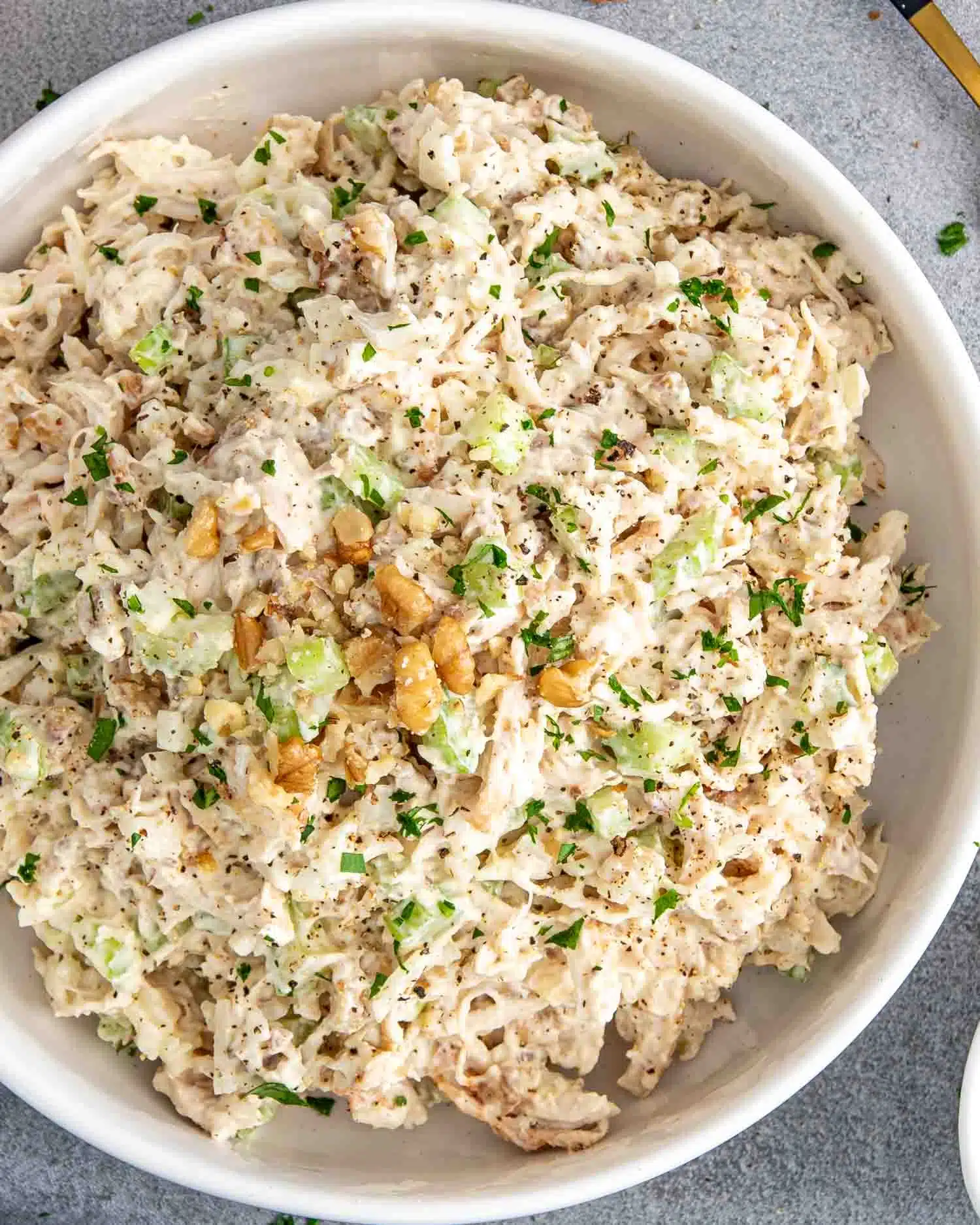 freshly made chicken salad in a white bowl garnished with a few extra crunchy walnuts.