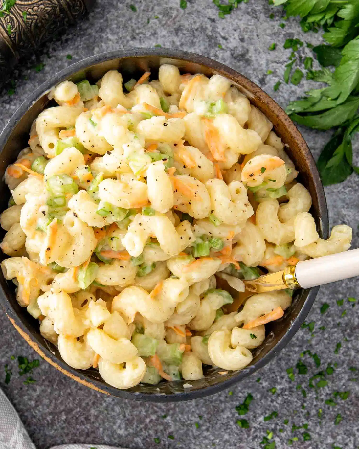 a brown bowl filled with freshly made macaroni salad and a fork inside.