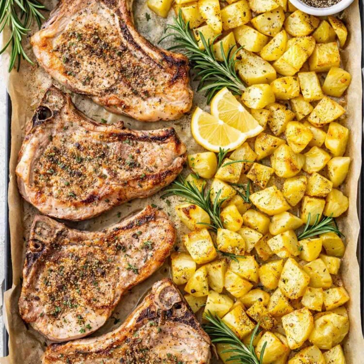 Oven baked pork chops with roasted potatoes on a sheet pan lined with parchment paper, seasoned and roasted until golden.