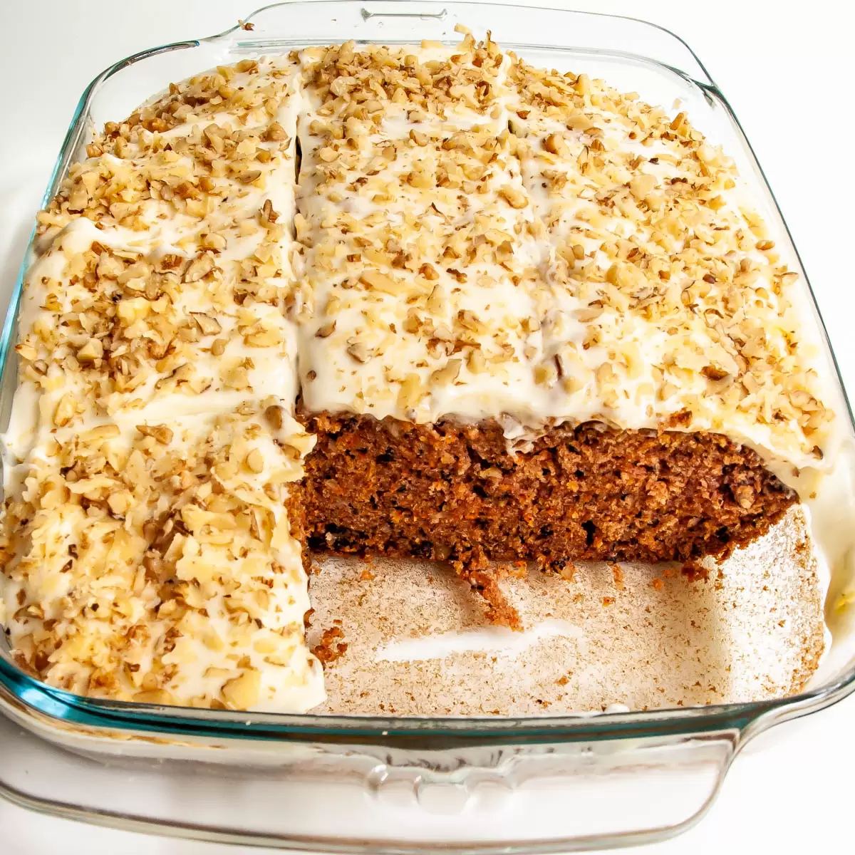 carrot cake in a baking dish topped with cream cheese icing and walnuts