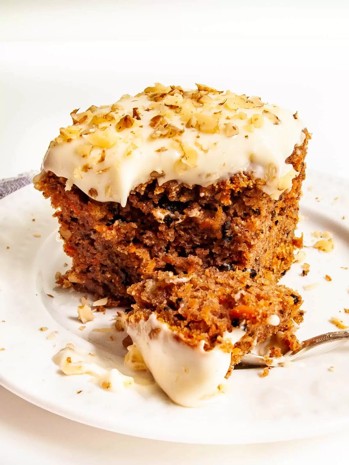slice of carrot cake on a white plate with a bite taken out of it