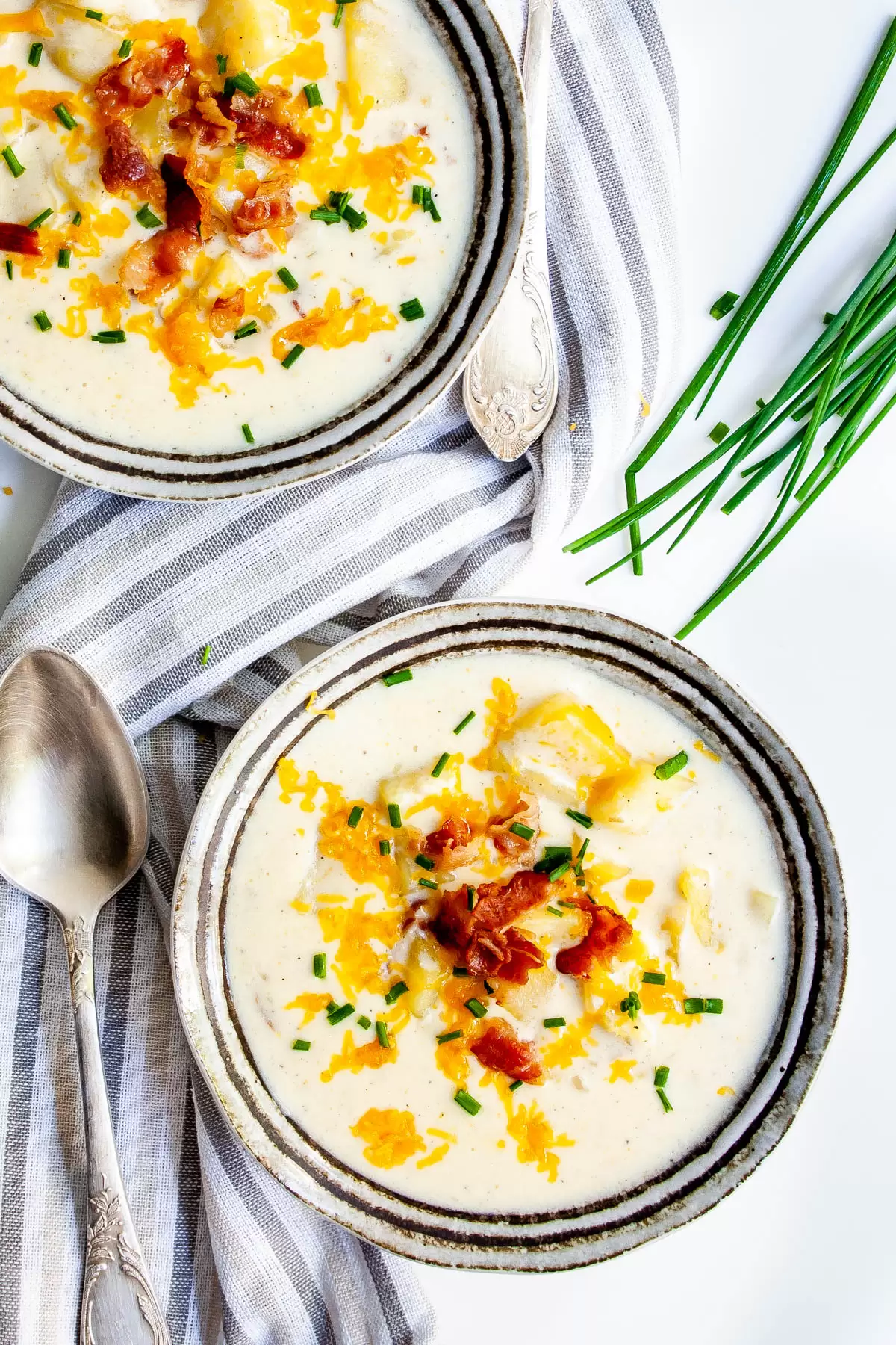 overhead shot of two bowls loaded with baked potato soup that are topped with cheese, bacon and chives