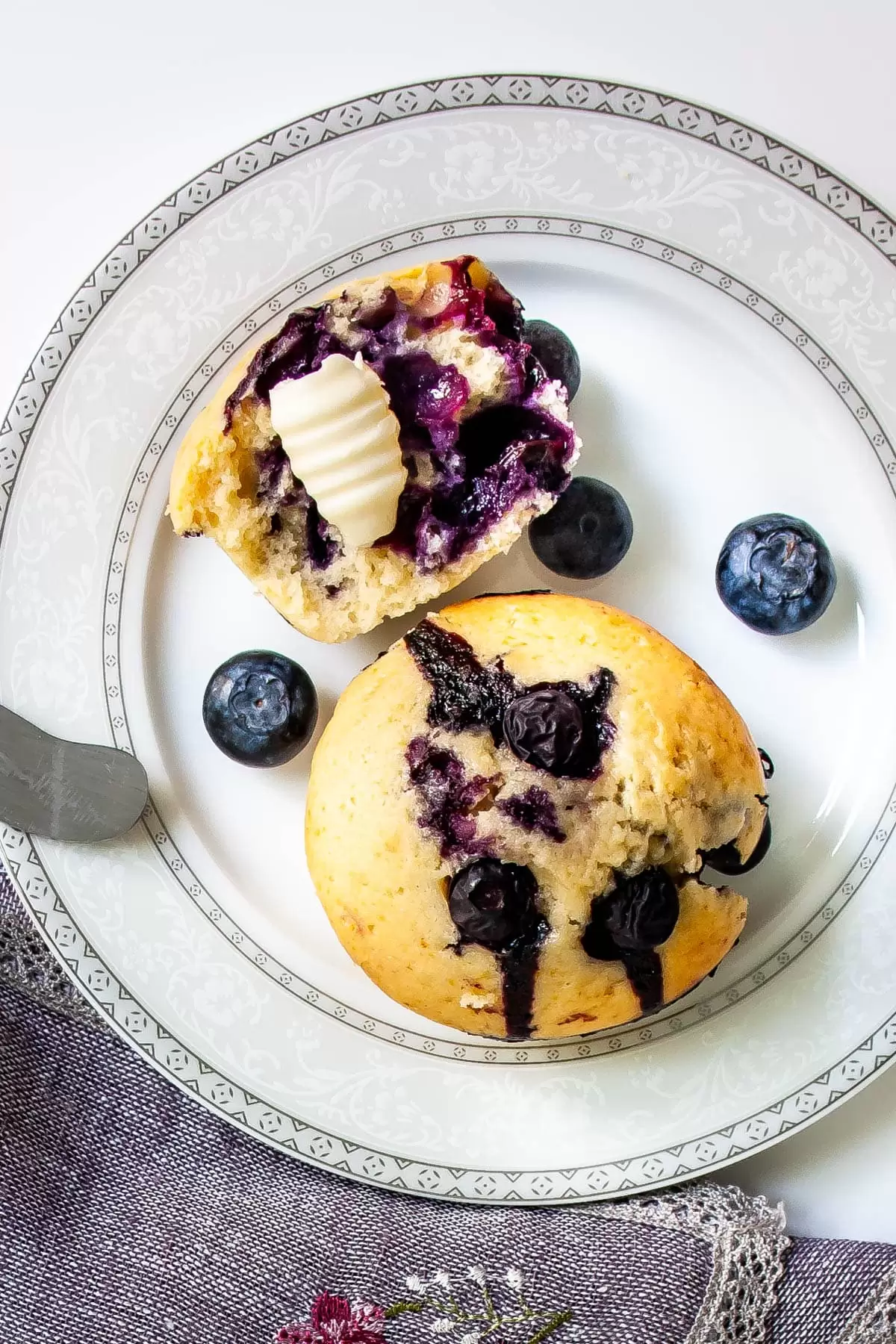 overhead shot of a white plate with a blueberry muffin and half a blueberry muffin