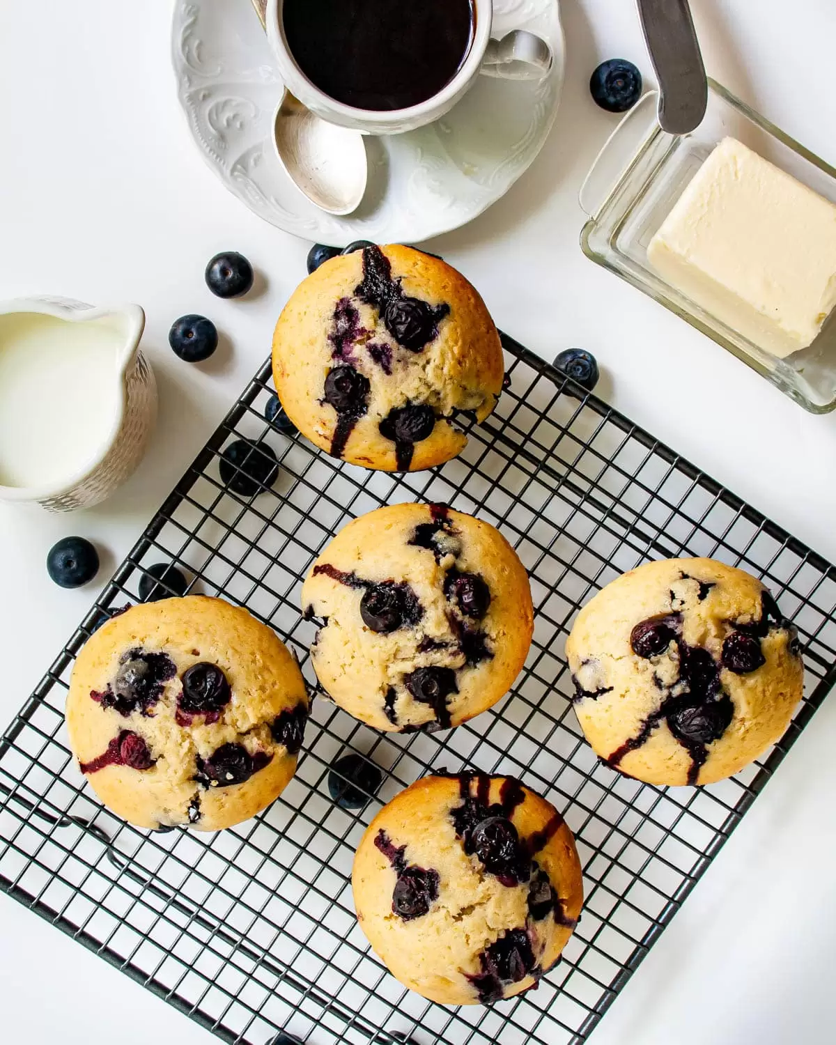 overhead shot of blueberry muffins on a cooling rack next to a cup of coffee