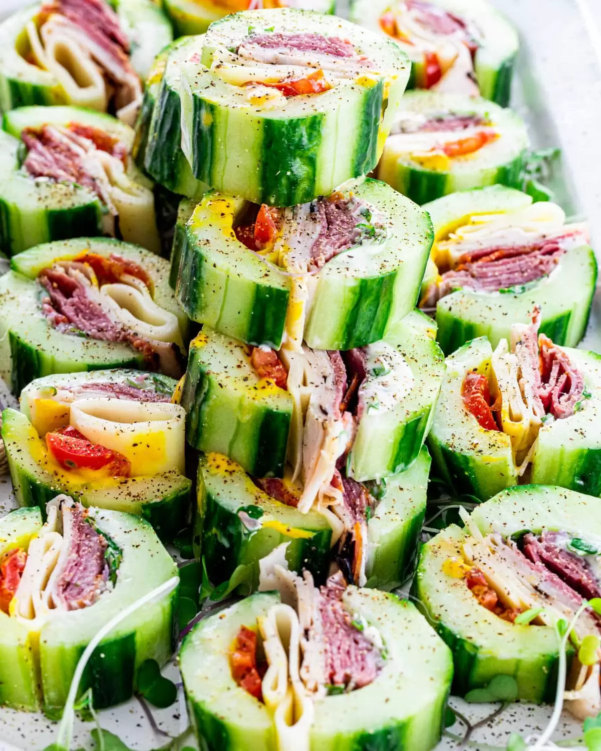 Finished cucumber sandwiches stacked on a white platter with black pepper sprinkled on top