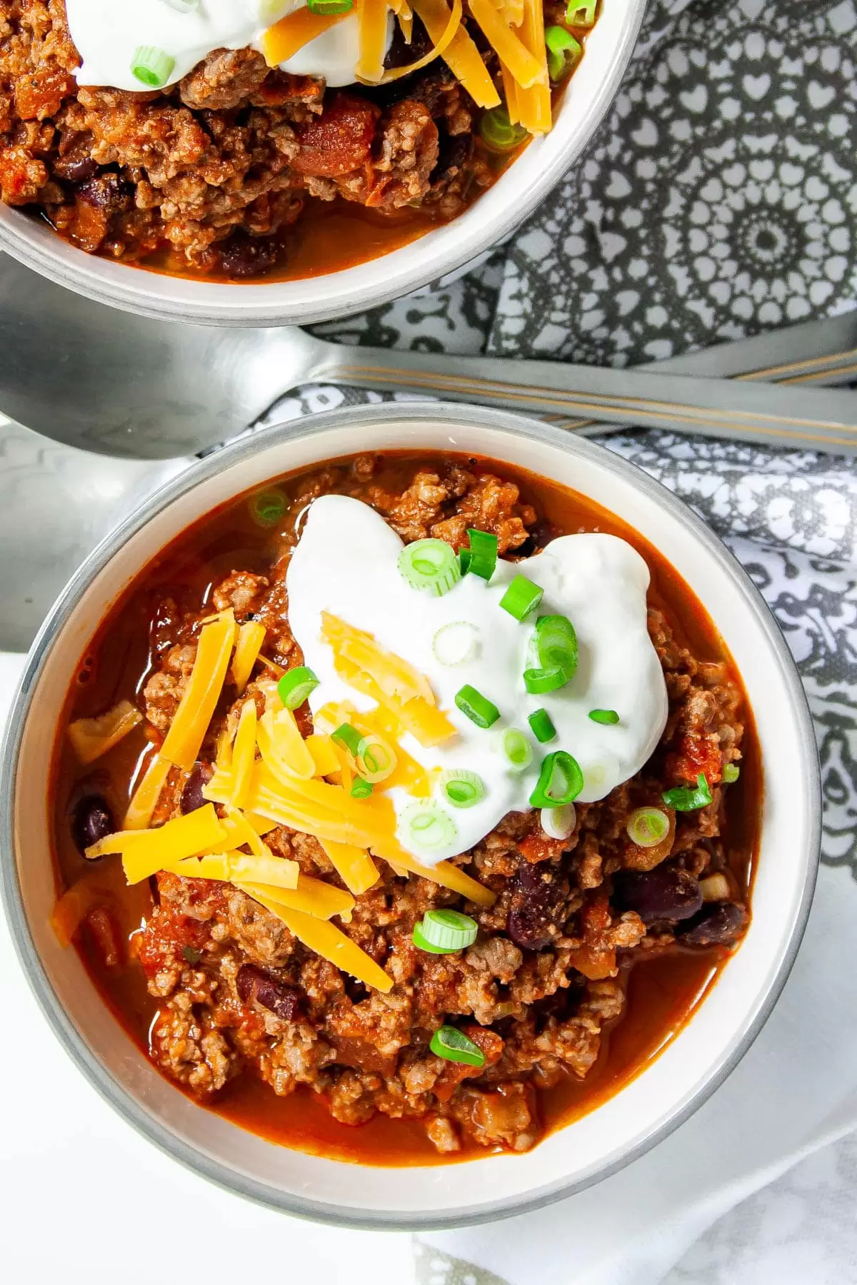 overhead shot of two bowl loaded with chili and topped with sour cream and cheddar cheese