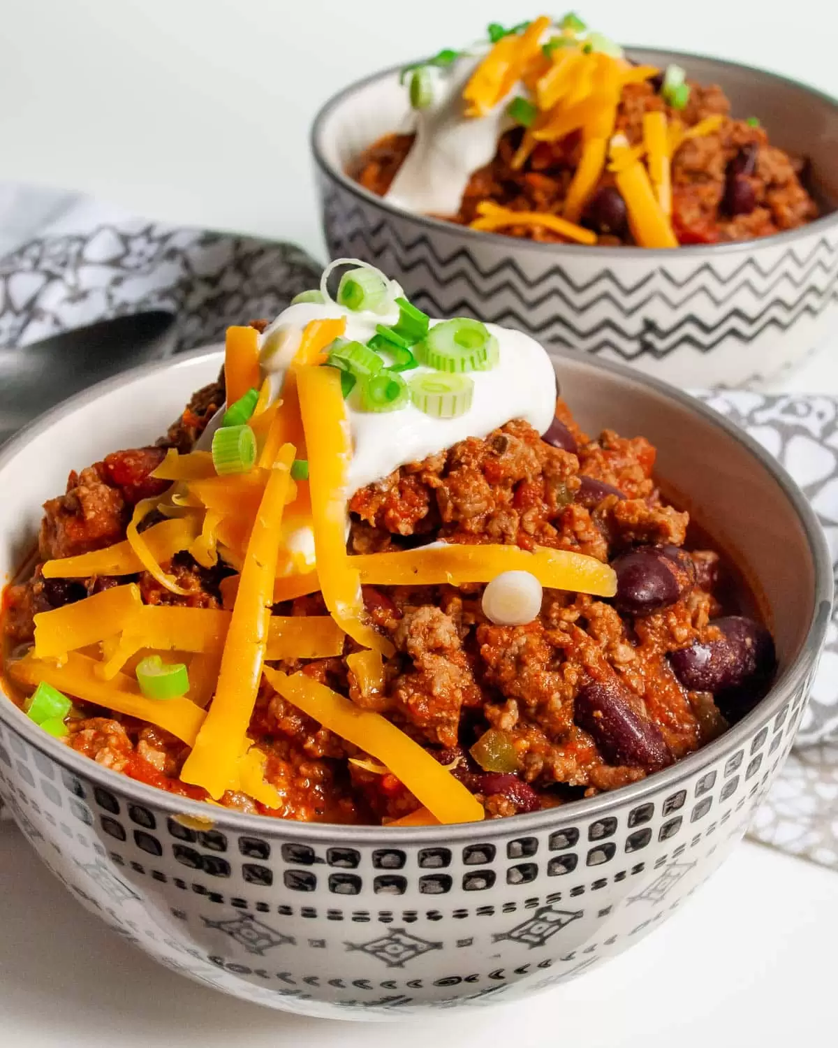 two bowls loaded with chili and topped with sour cream and cheddar cheese