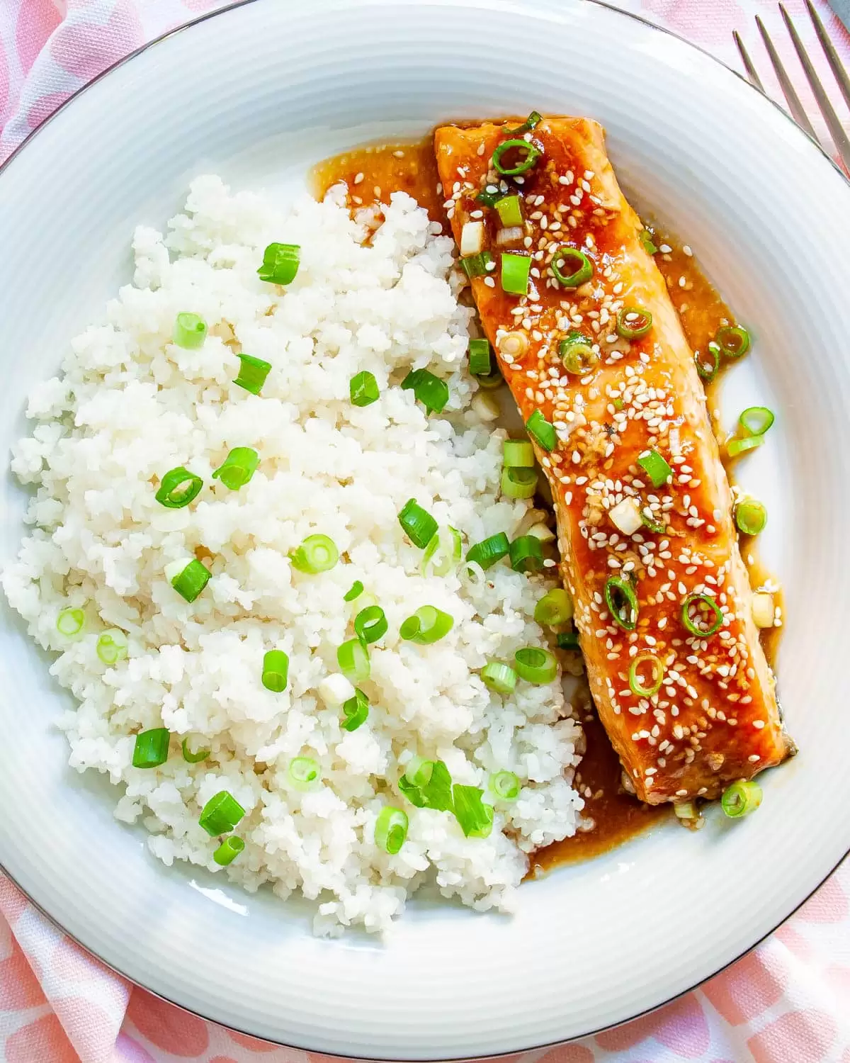 overhead shot of baked teriyaki salmon and coconut rice on a white plate garnished with green onions