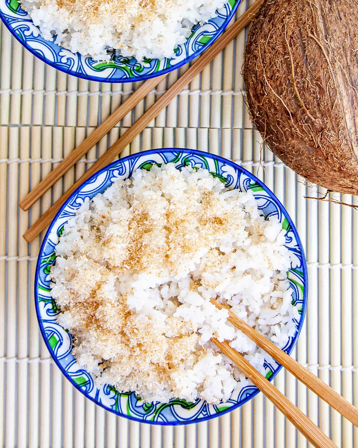 overhead shot of two bowls loaded with coconut rice next to a coconut