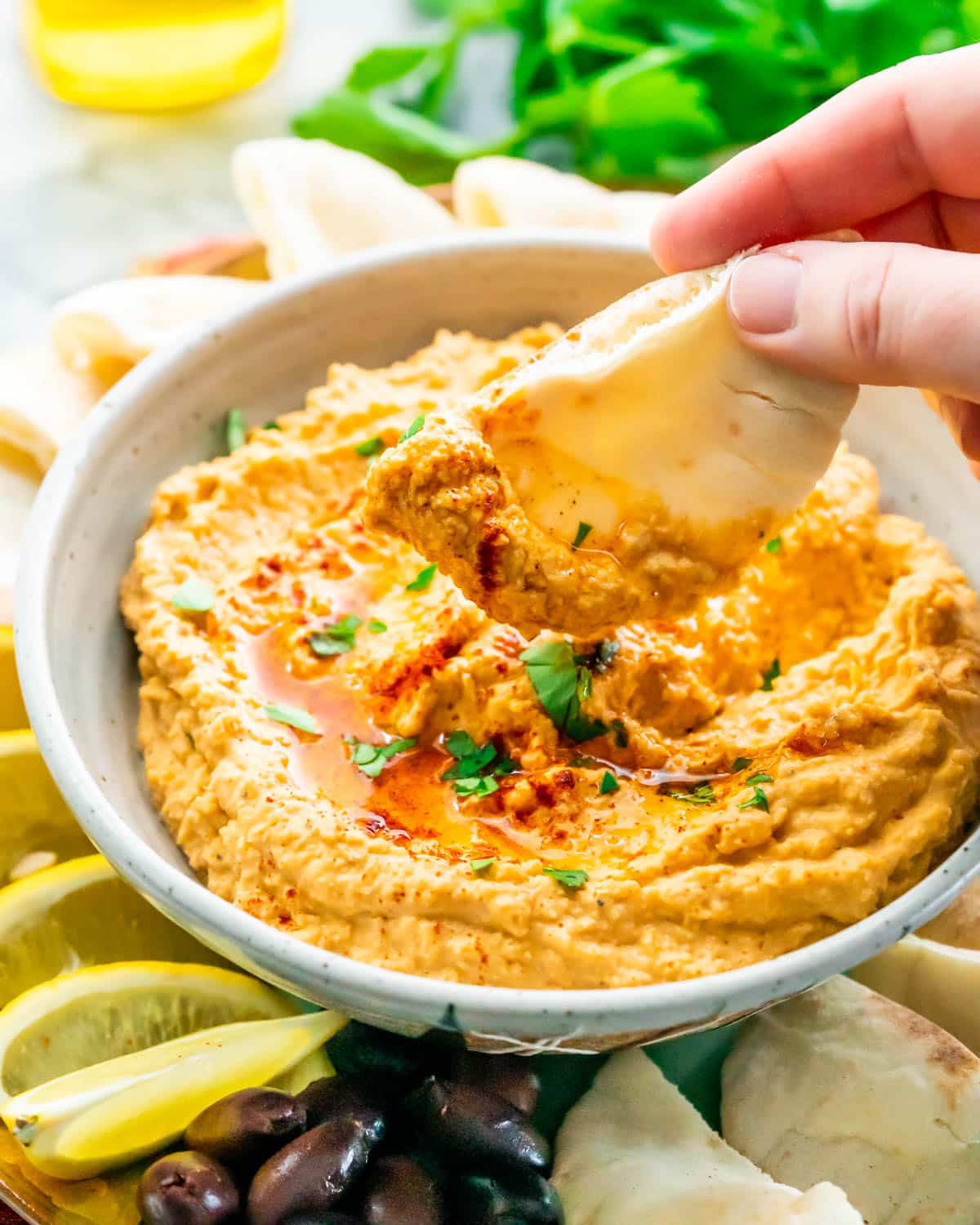 a hand scooping out some hummus with a pita chip