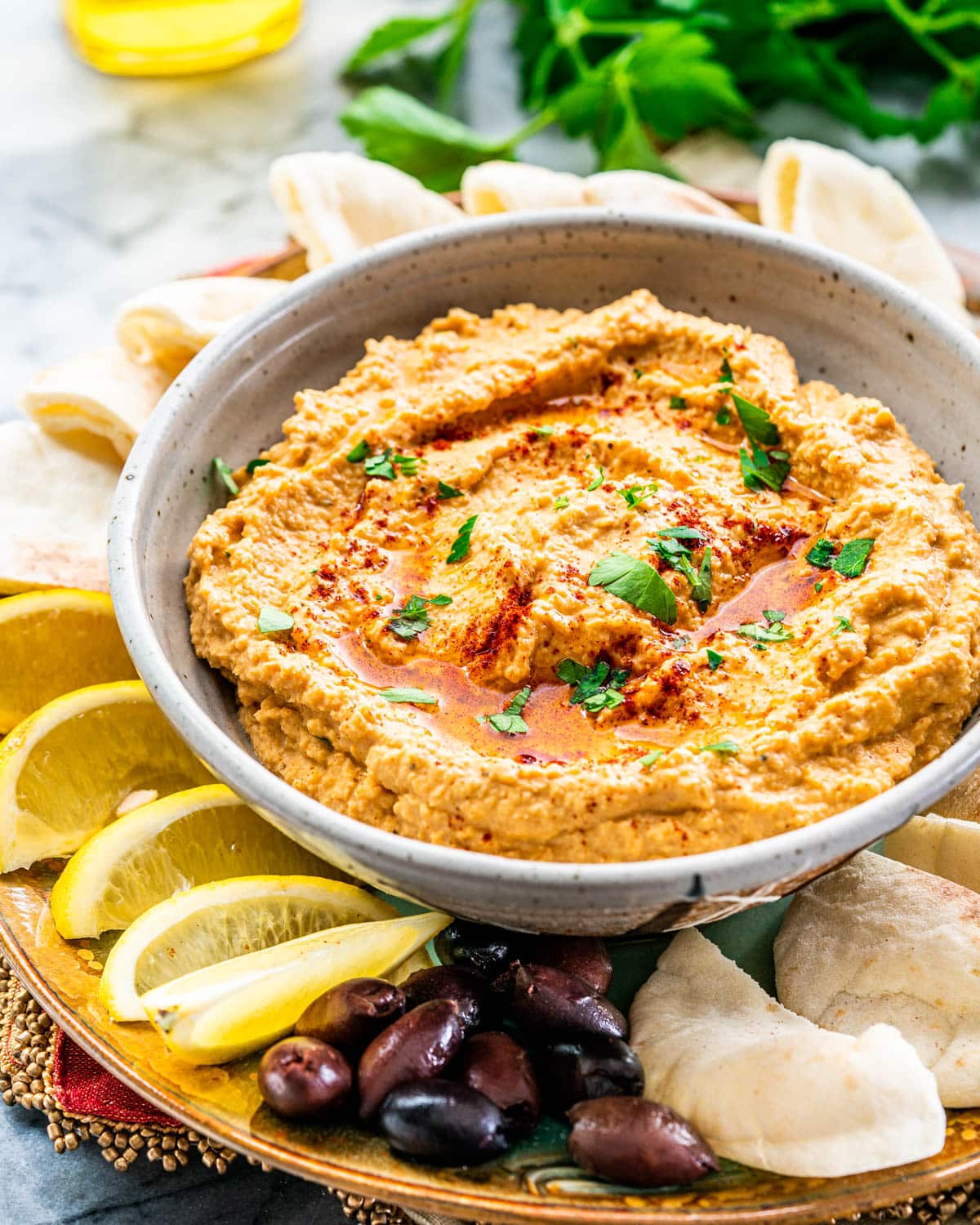 hummus in a bowl surrounded by pita chips, lemon wedges and olives