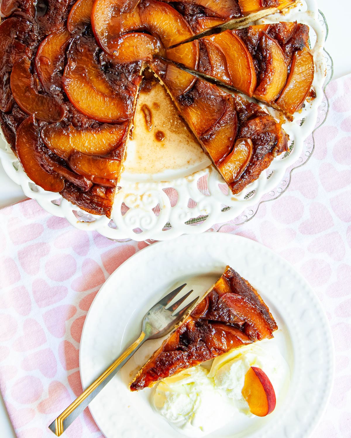 overhead shot of half a Peach Upside Down Cake on a white plate and a slice of cake on a white plate