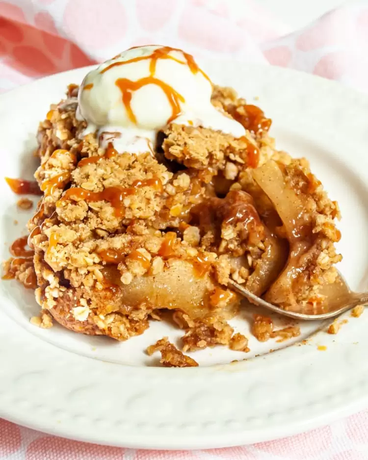 a slice of apple crisp on a plate with ice cream and caramel sauce