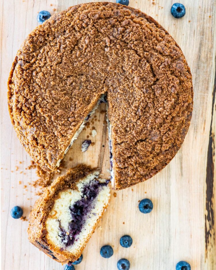 overhead shot of blueberry coffee cake with a slice cut out of it on a cutting board