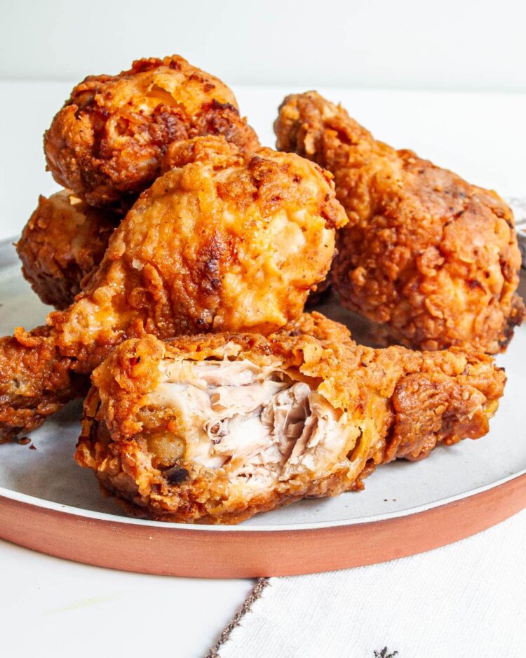 a stack of crispy fried chicken drumsticks with one drumstick having a bite taken out of it