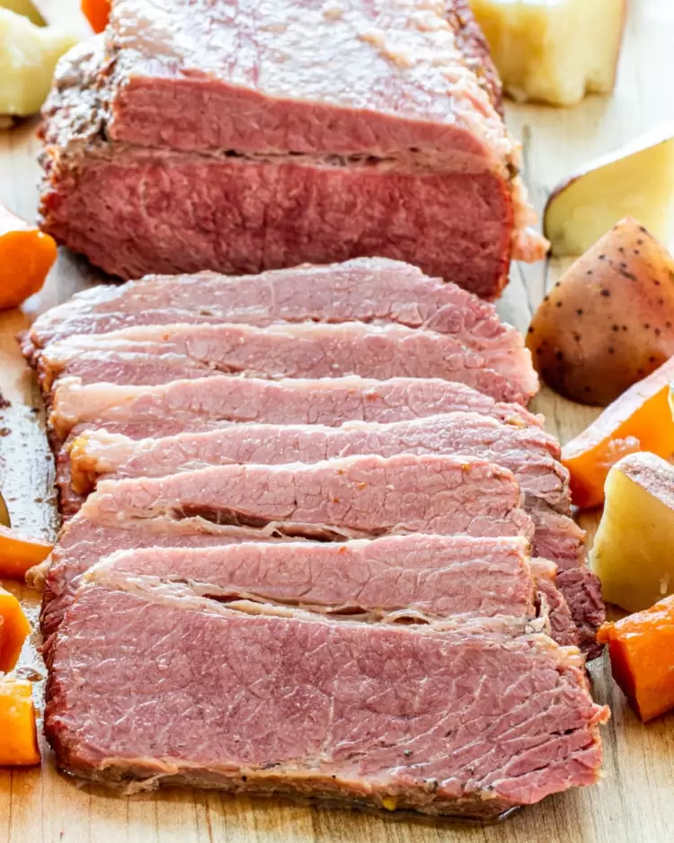 corned beef on a cutting board surrounded by potatoes and carrots