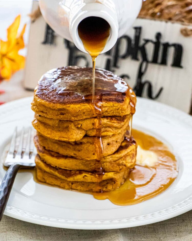 pouring of maple syrup over pumpkin pancakes