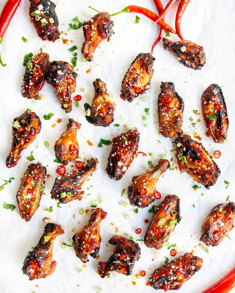 baked chicken wings on parchment paper garnished with chili peppers and green onions