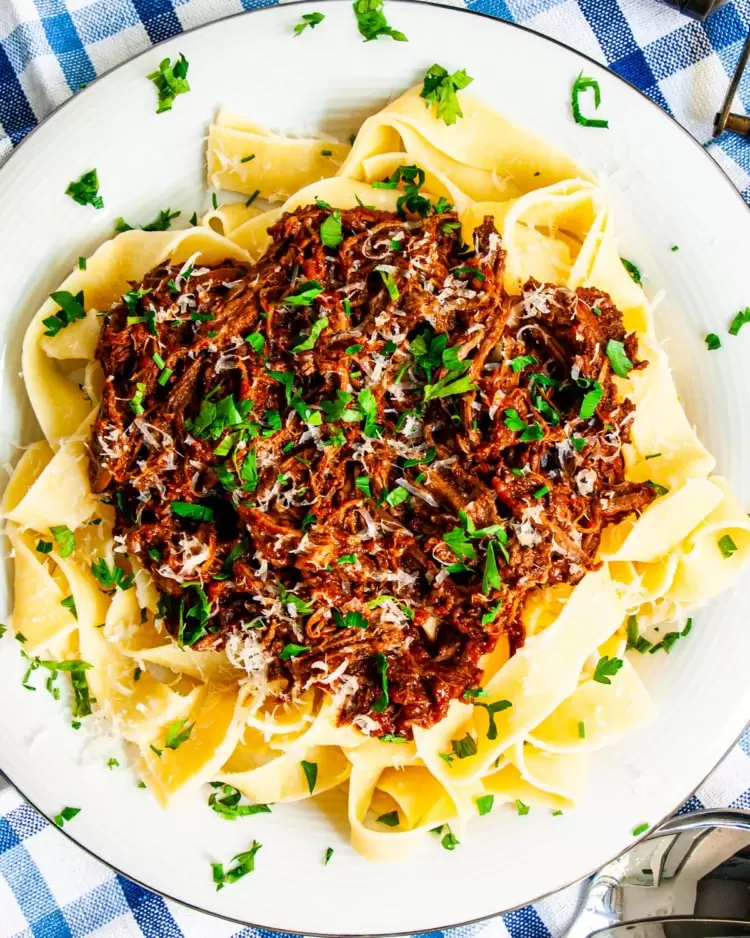 overhead shot of beef ragu over a plate of fettuccine garnished with parmesan cheese and parsley