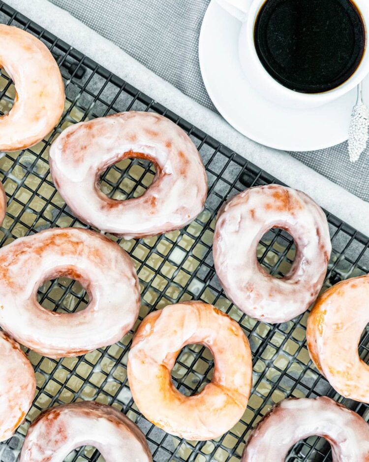 krispy kreme donuts on a cooling rack next to a cup of coffee