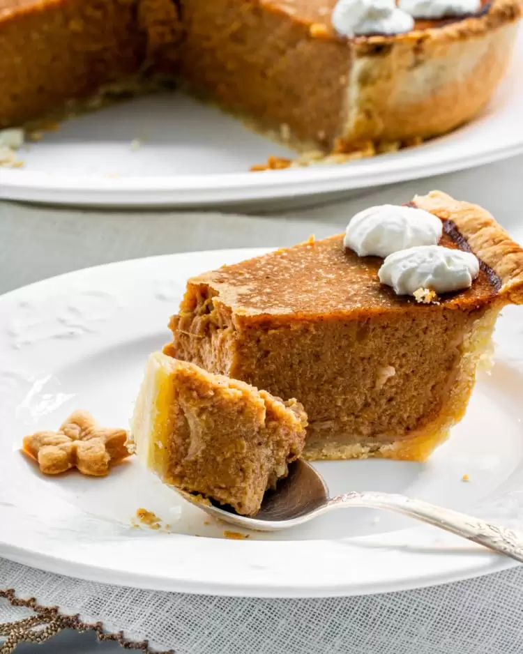 a slice of pumpkin pie on a white plate with a bite in a spoon