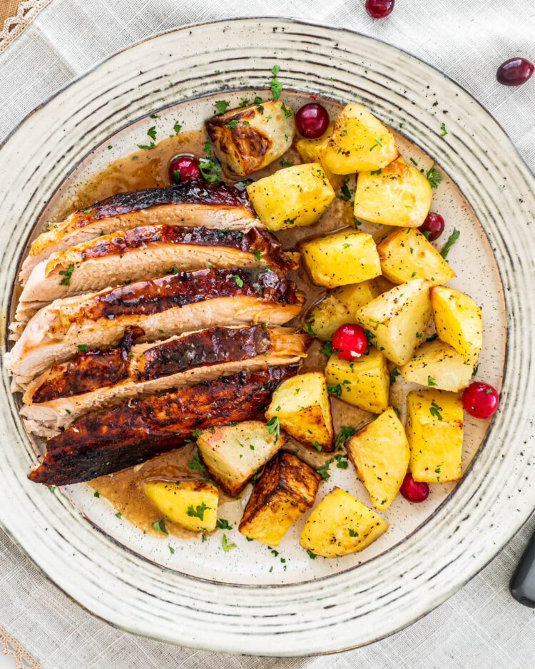 overhead shot of sliced turkey breast with roasted potatoes on a beige plate