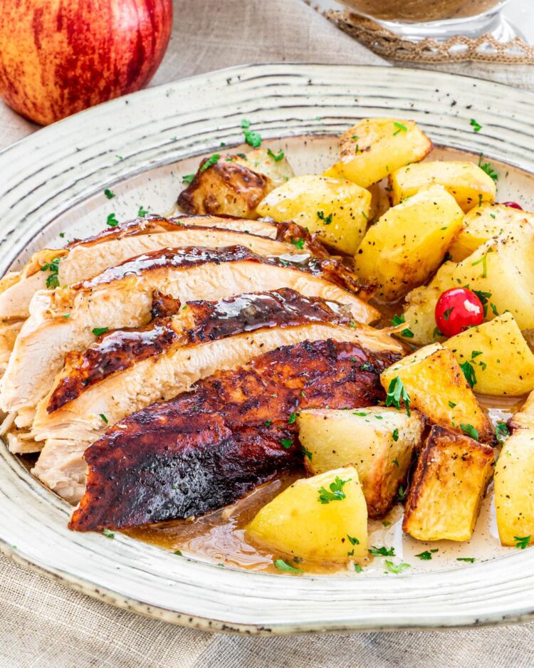 slices of turkey with gravy and roasted potatoes on a beige plate