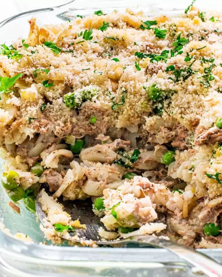 a serving spoon inside a tuna noodle casserole in a baking dish