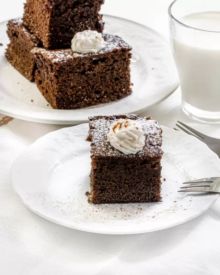 a slice of gingerbread cake with a dollop of whipped cream with a glass of milk in the background