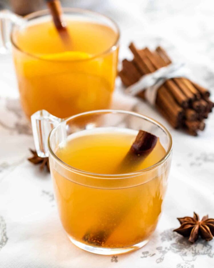 two mugs filled with hot mulled cider with a cinnamon stick in each mug