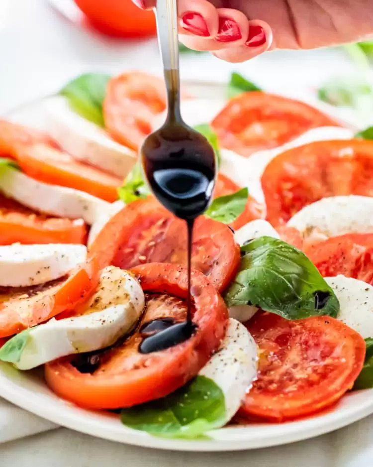 a spoon with balsamic glaze drizzling some over caprese salad