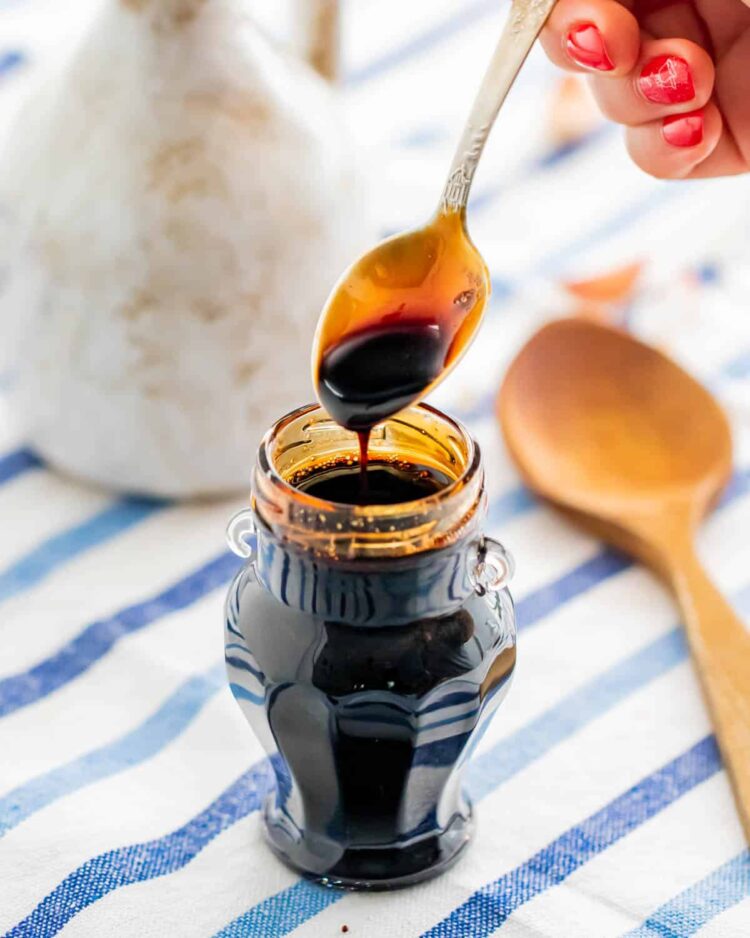 a jar filled with balsamic glaze and a hand holding a spoon over the jar