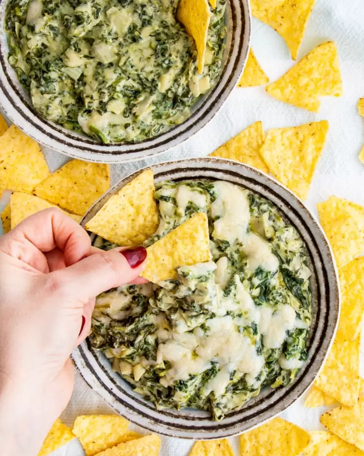 overhead shot of two bowls with spinach dip surrounded by tortilla chips