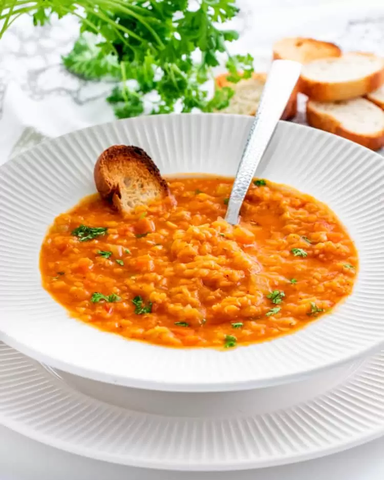 lentil soup in a white plate with toasted bread and a spoon 
