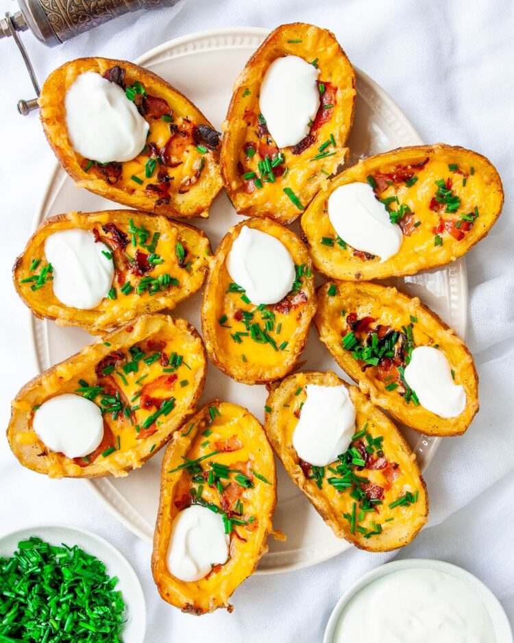 overhead shot of potato skins on a white platter garnished with sour cream, bacon and chives