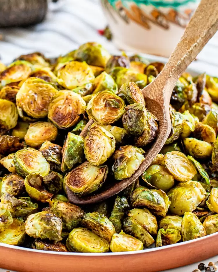 a spoon holding some roasted brussels sprouts over a plate loaded with them