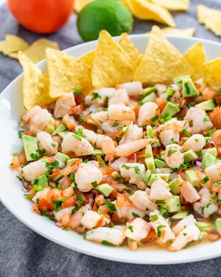 a white bowl full of shrimp ceviche and tortilla chips on the side
