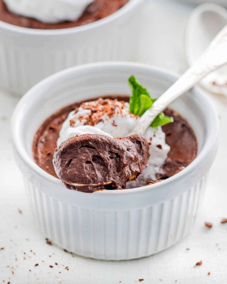 avocado chocolate mousse in a white ramekin with a spoon in it topped with whipped cream